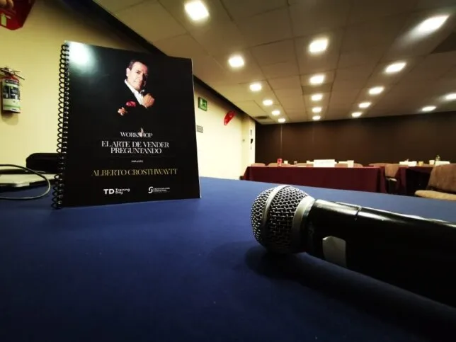 Un micrófono y material de trabajo de Alberto sobre ventas en una sala de conferencias lista para el curso de liderazgo